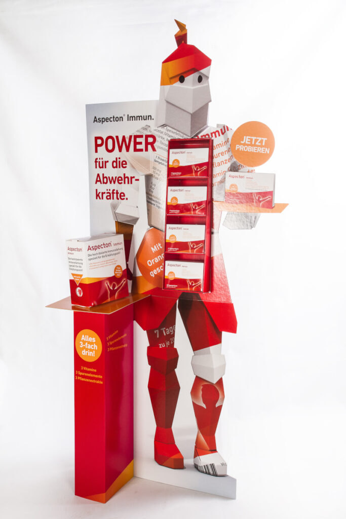 Beispiel eines Bodenaufstellers, bestehend aus einer Rückwand mit großflächigem Aufdruck, sowie einem kleinen Tisch auf dem eine Produktpackung steht.