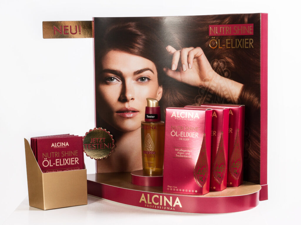 Beispiel für ein Thekendisplay, bestehend aus einer Präsentationsfläche für ein Kosmetikprodukt und einer bedruckten Rückwand. Abgesetzt ist ein Fach für Flyer abgebildet.