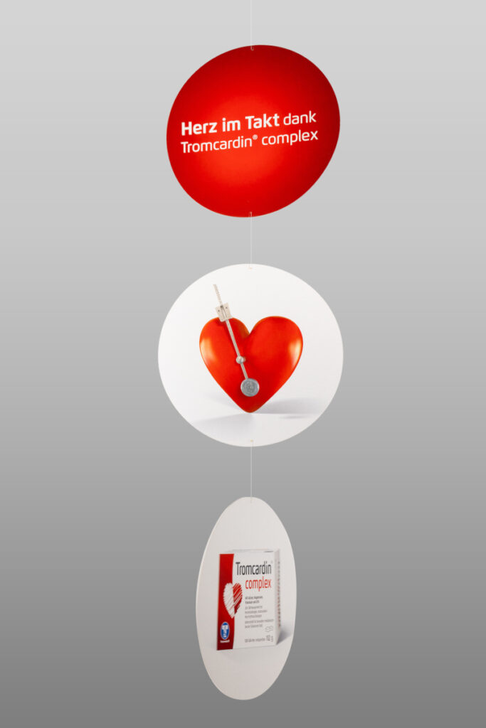 Beispiel für einen Deckenhänger zur Dekoration. Der Deckenhänger besteht aus drei mit Schnüren verbundenen, kreisförmigen Elementen, die jeweils beschriftet oder mit einem Bild bedruckt sind.