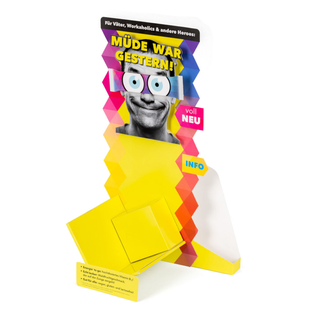 Beispiel für ein Thekendisplay. Das Produkt ist in einer Art Schütte diagonal gelagert, die Ränder sind gezackt, das Display ist bunt bedruckt.