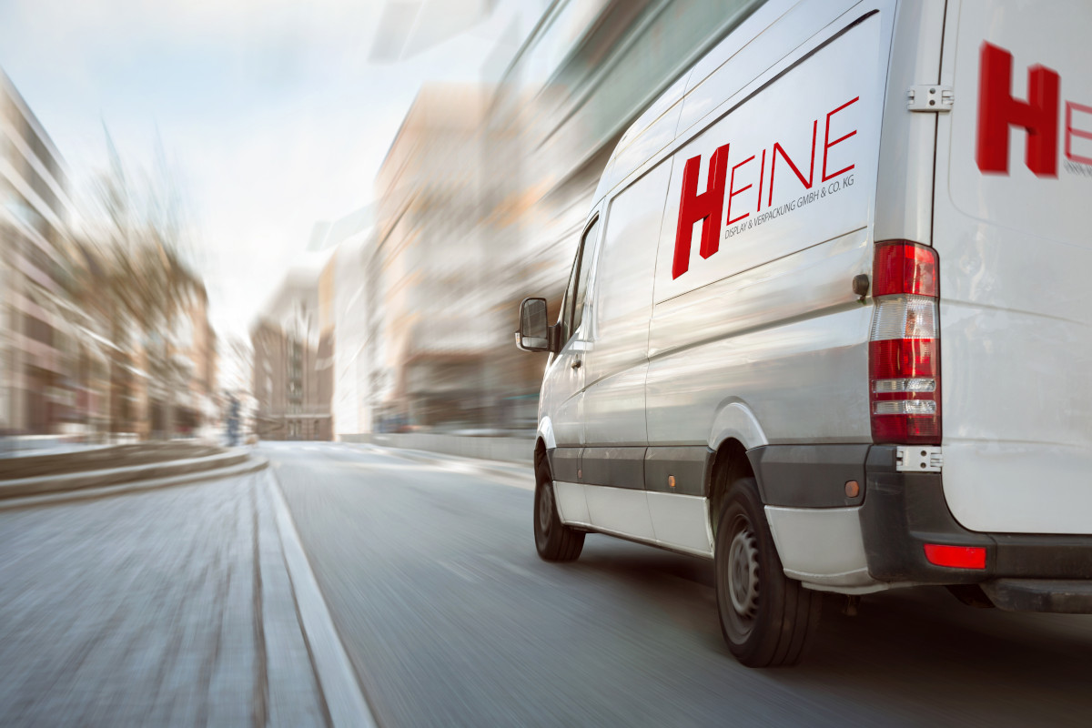 Ein weißer Lieferwagen mit dem Heine-Logo fährt über eine Straße